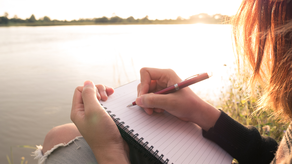 A girl starting to write something by the lake. Write gratitude